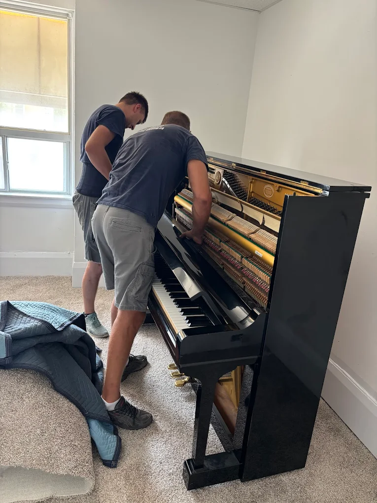 Professional piano movers disassembling upright piano
